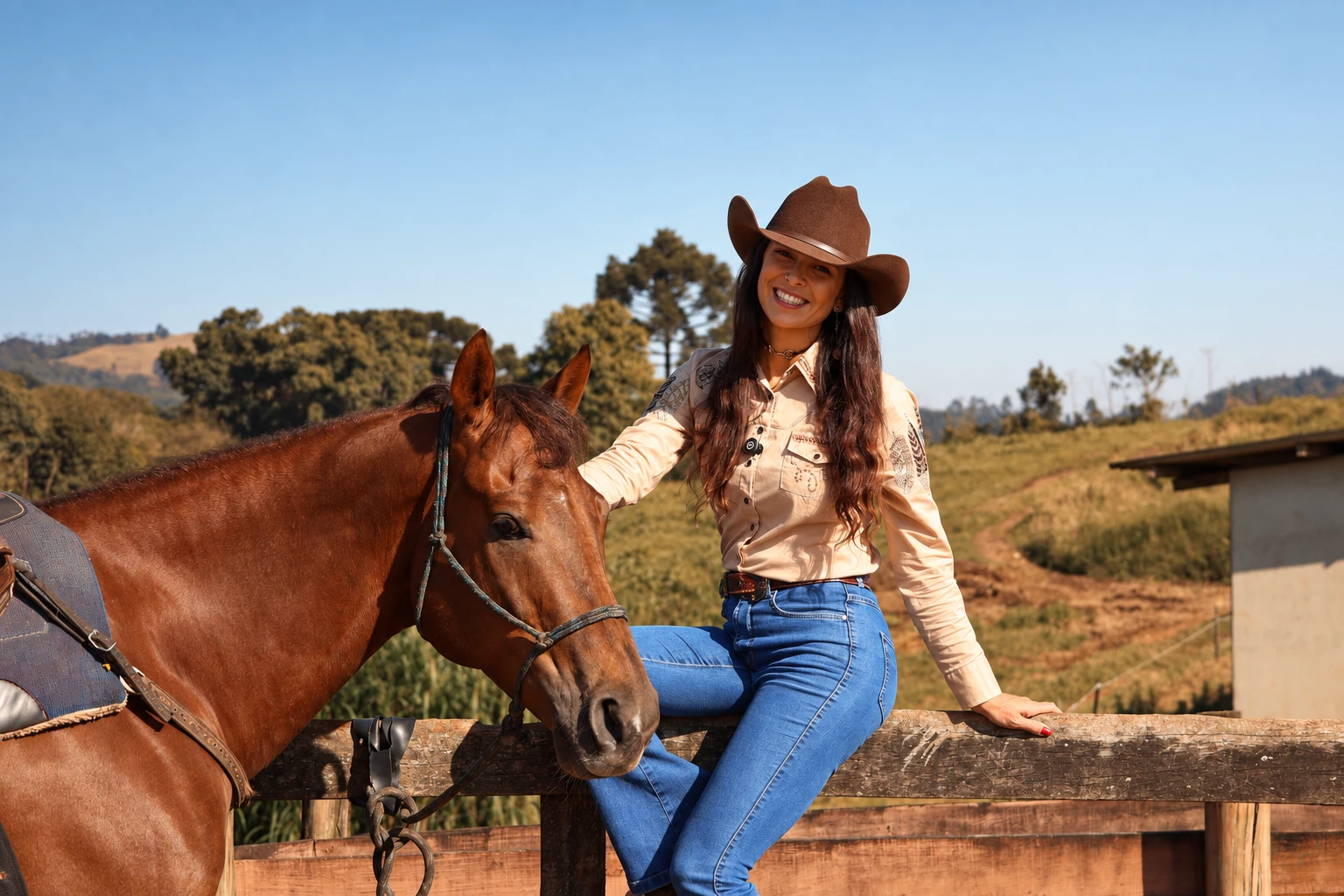 Vanessa Castro sorrindo, de chapéu, sentada na cerca ao lado do seu cavalo, com a fazenda ao fundo